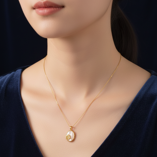 Gold necklace with a pendant on a person wearing a dark blue top against a black background