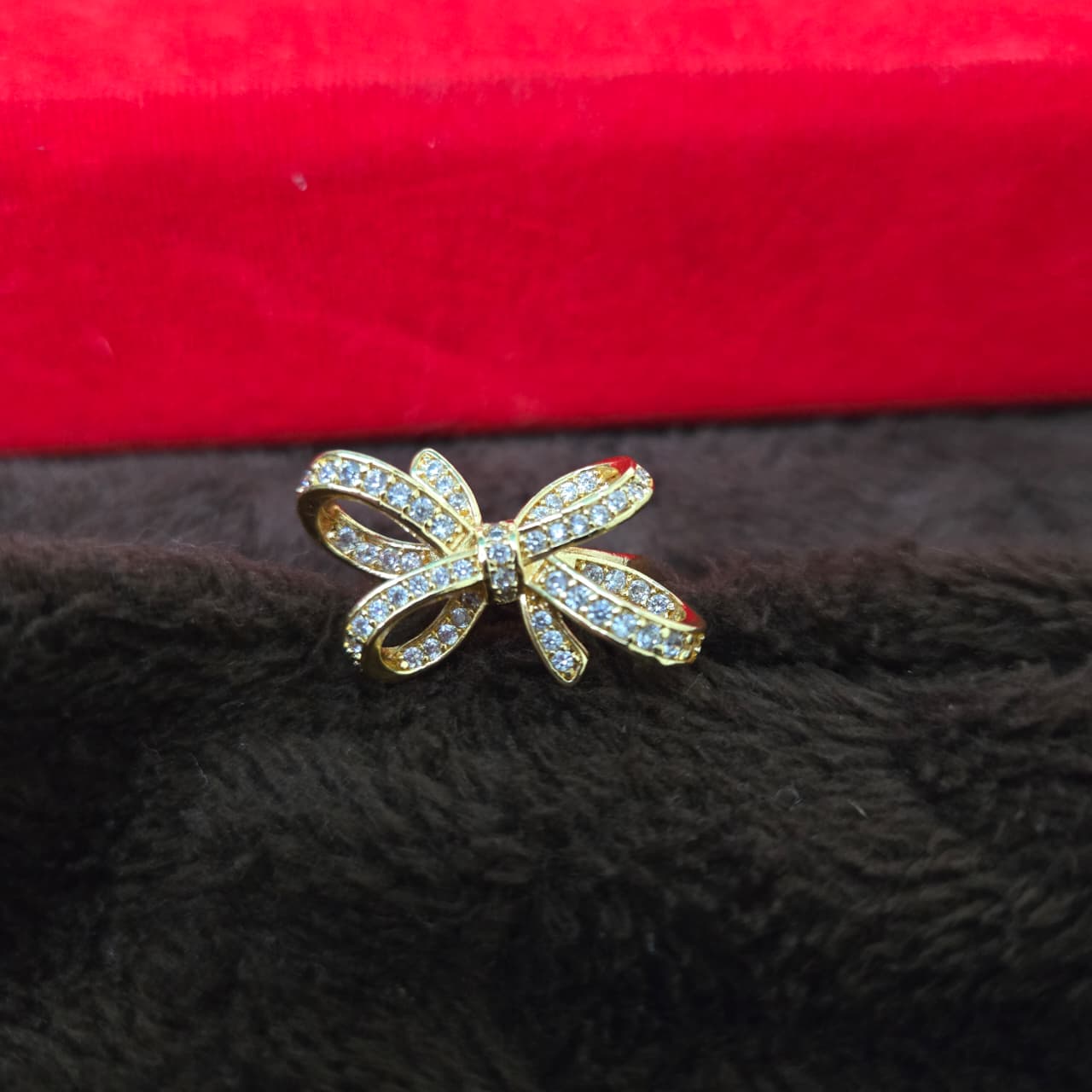 Gold bow-shaped ring with gemstones on a black and red textured fabric background