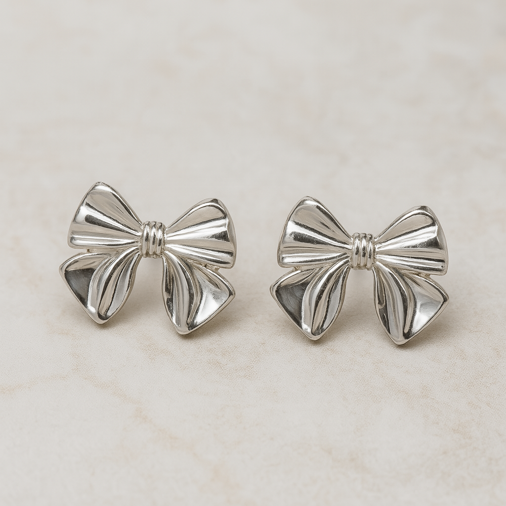 Silver bow-shaped earrings on a light beige background