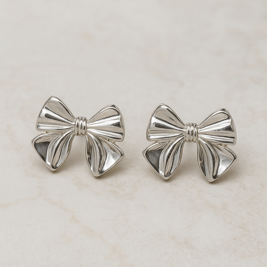 Silver bow-shaped earrings on a light beige background
