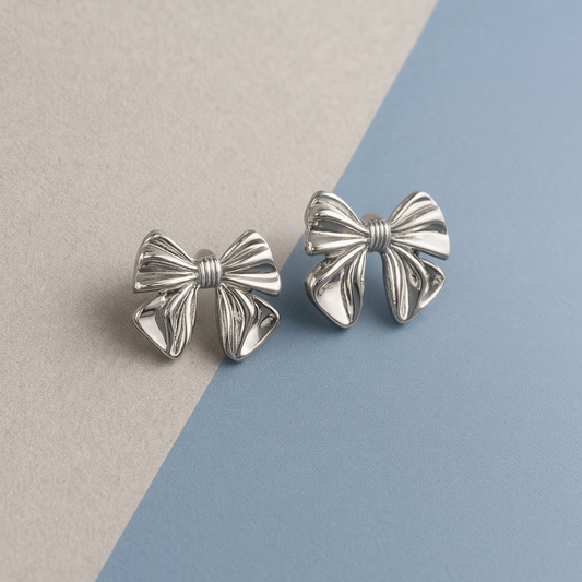 Silver bow-shaped earrings on a two-tone beige and blue background