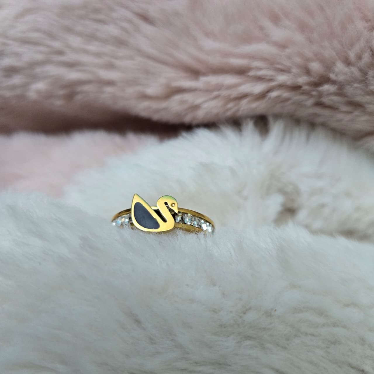 Gold ring with black stone on a fluffy pink and white background