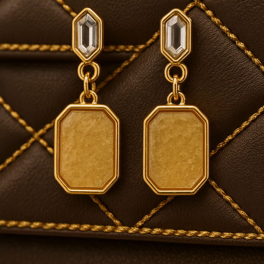Gold earrings with a textured design on a brown quilted background