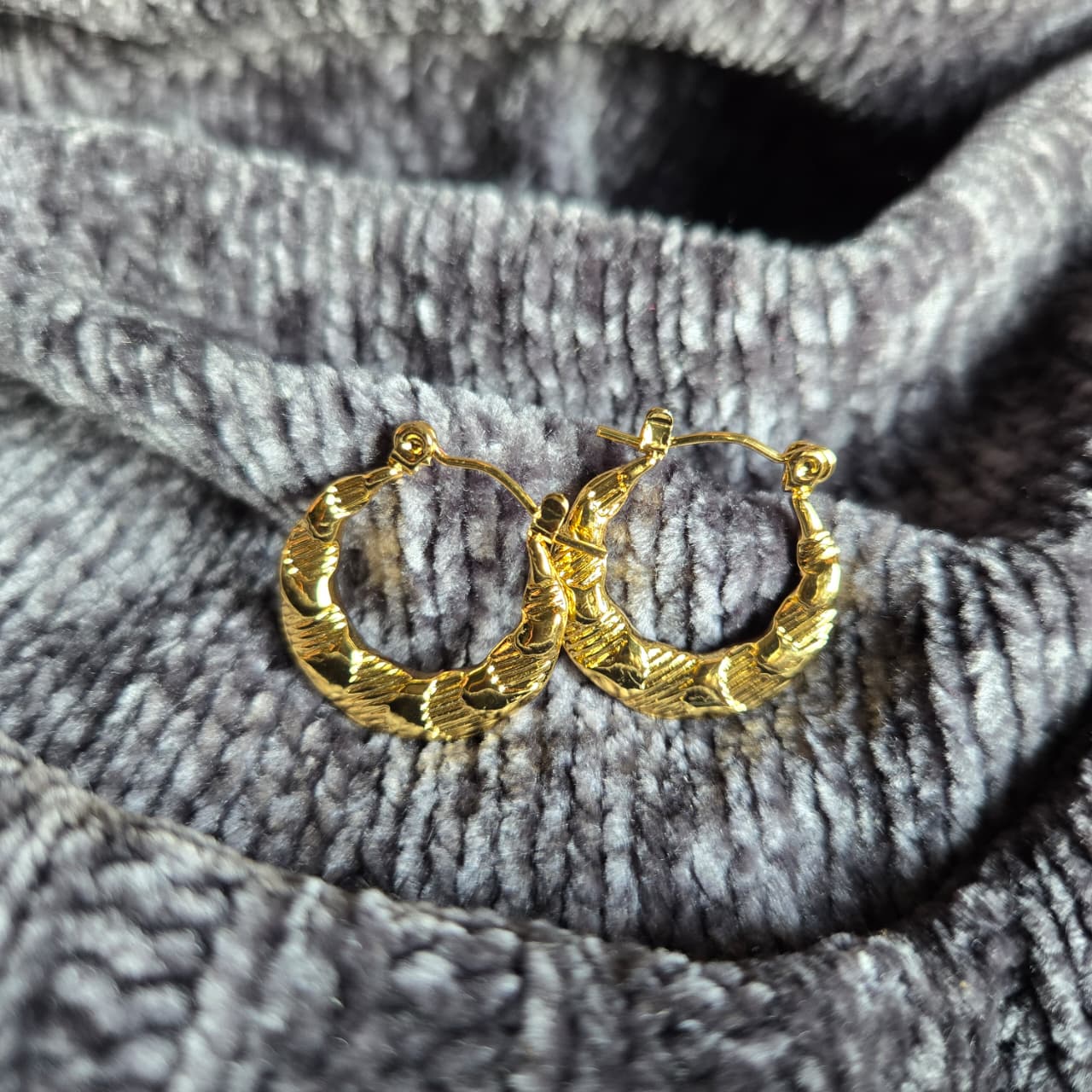 Gold hoop earrings on a textured gray fabric background