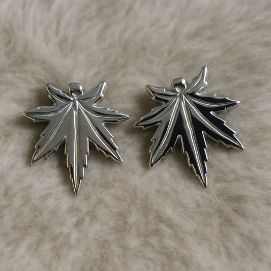 Two silver leaf-shaped pendants on a beige surface