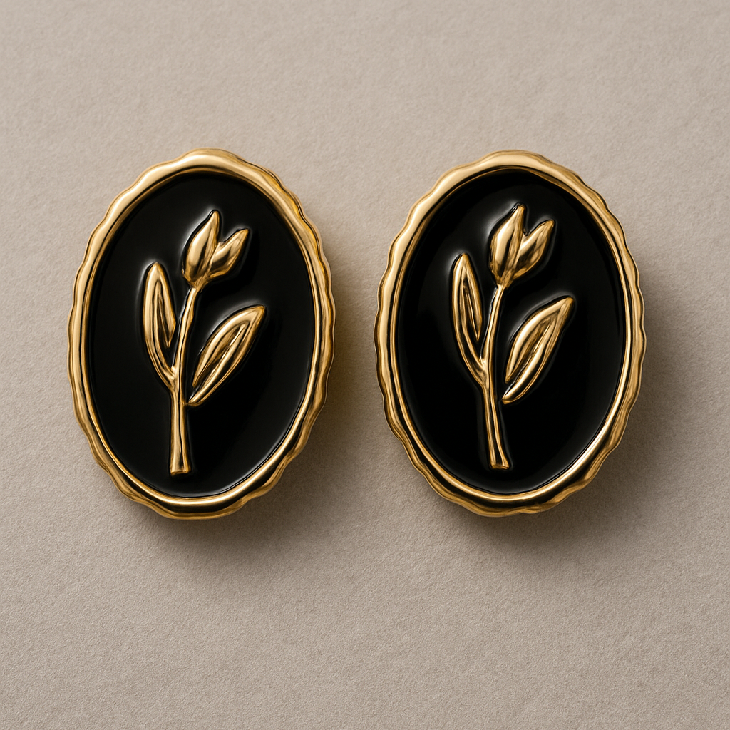 Elegant oval black and gold stud earrings with a raised botanical design on a glossy enamel finish