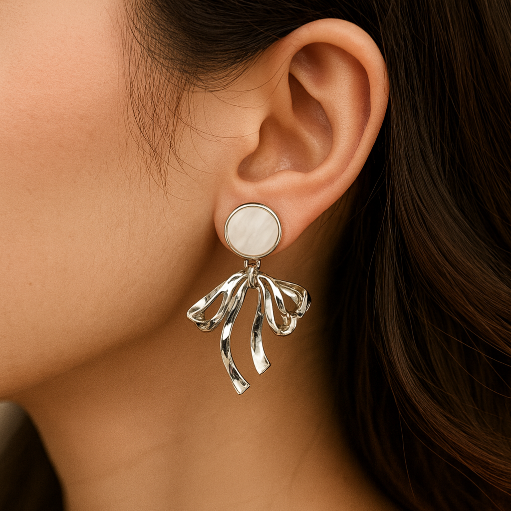 Silver bow-shaped earring with a round gemstone worn by a person.