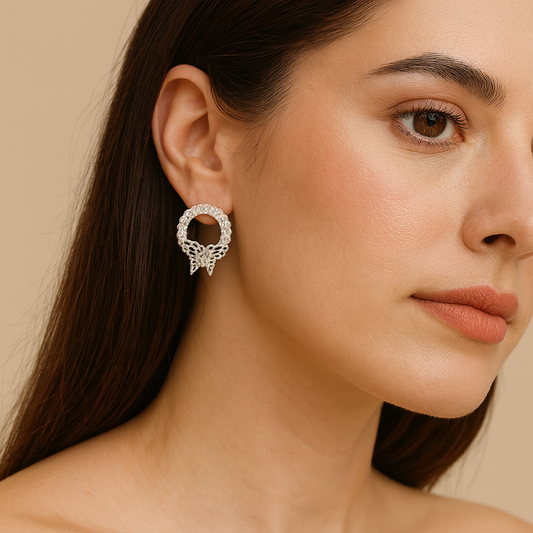 Close-up of a woman wearing silver circular earrings adorned with a delicate butterfly design, against a neutral beige background.