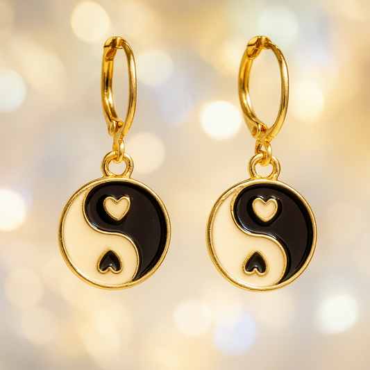 Gold earrings with black yin yang symbols on a blurred gold background