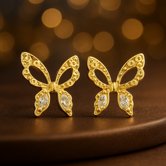 Gold butterfly earrings with gemstones on a brown surface and blurred background
