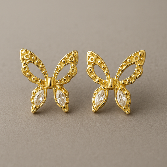 Gold butterfly earrings with gemstones on a brown surface and blurred background