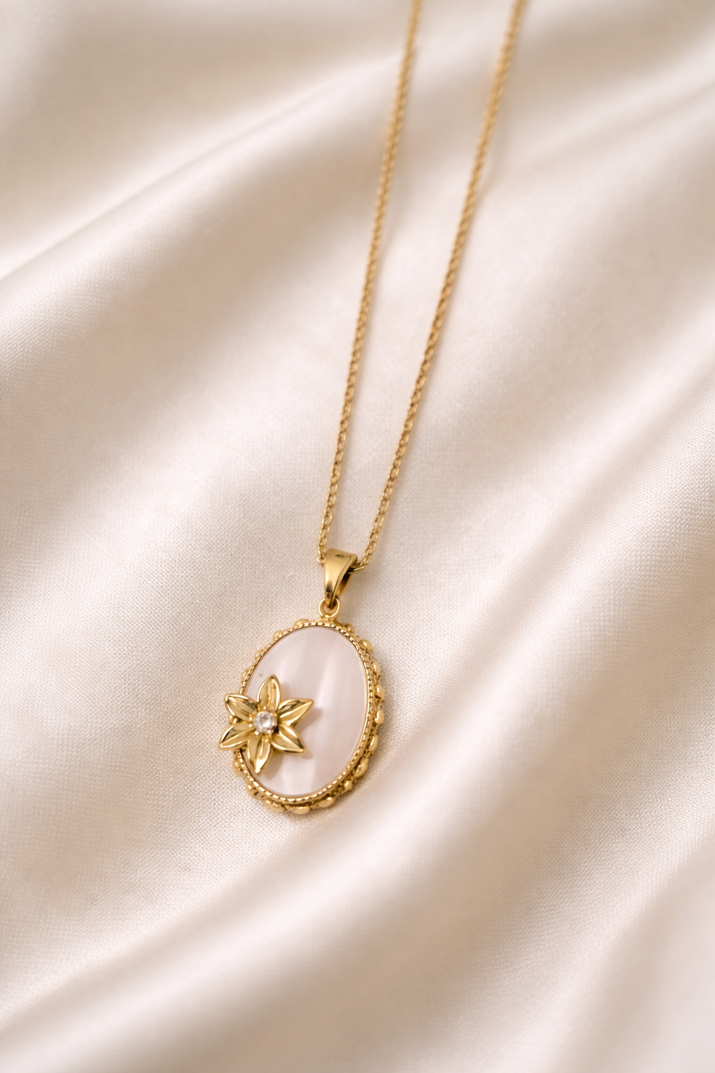 Gold necklace with a pendant on a white cloth background.