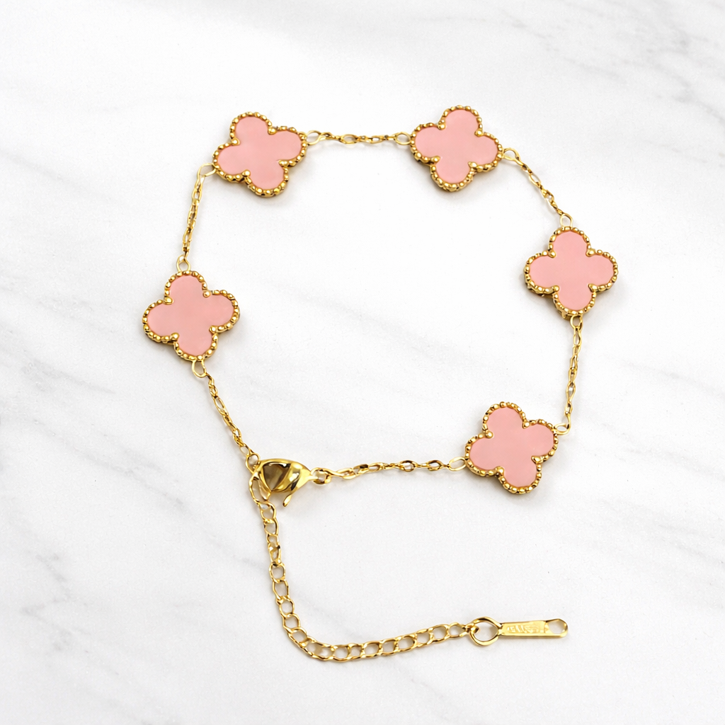 a bracelet with delicate pink clover-shaped charms framed in a radiant gold finish on a white marble background.