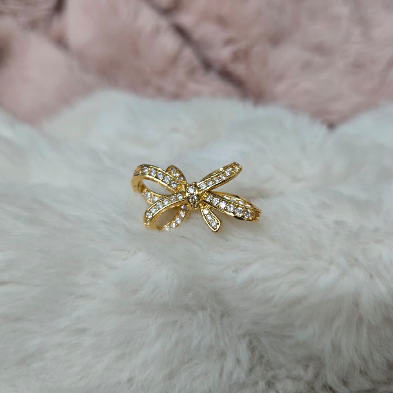 Gold bow-shaped ring with gemstones on a fluffy white surface