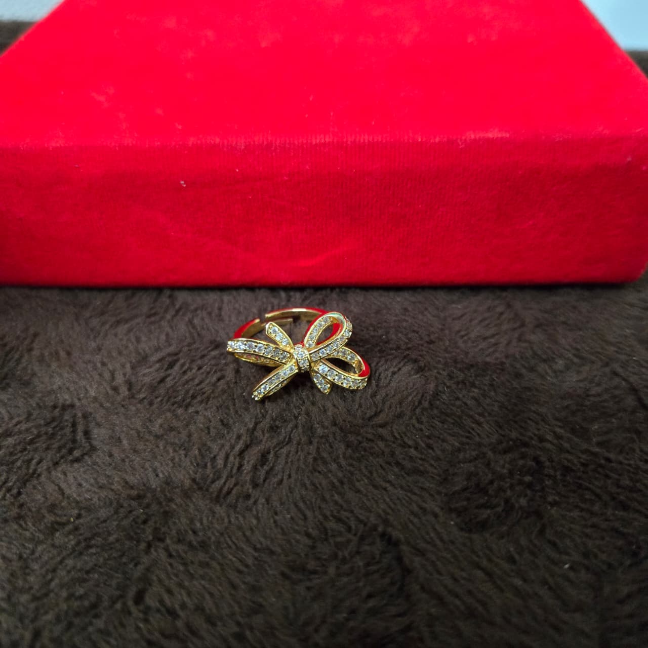 Gold bow-shaped ring with red accents on a textured surface