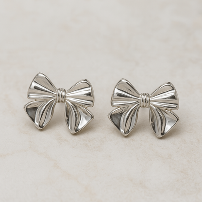 Silver bow-shaped earrings on a light beige background