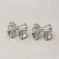 Silver bow-shaped earrings on a light beige background