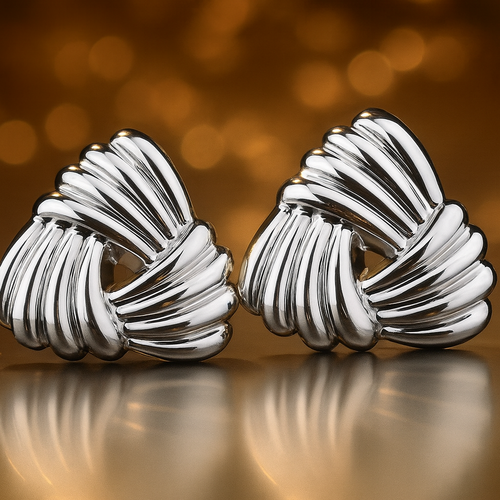 Pair of silver knot earrings on a reflective surface with a blurred golden background
