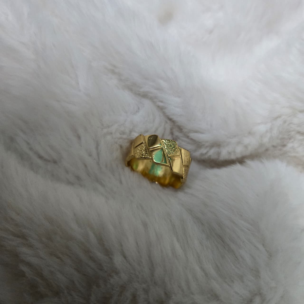 Gold ring with green gemstone on a white fur surface