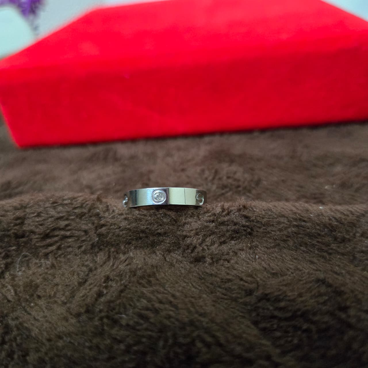 Silver ring with a diamond on a brown surface with a red box in the background