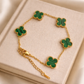 A timeless gold-tone station bracelet featuring elegant clover-shaped charms in rich green malachite-style detailing on a book.