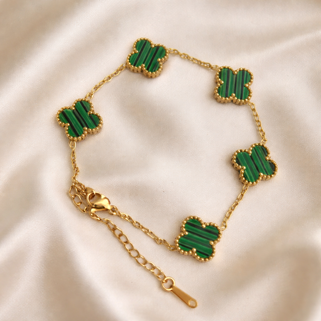 A timeless gold-tone station bracelet featuring elegant clover-shaped charms in rich green malachite-style detailing on a white cloth.