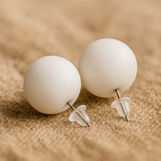 Pair of white spherical earrings on a beige surface