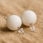 Pair of white spherical earrings on a beige surface