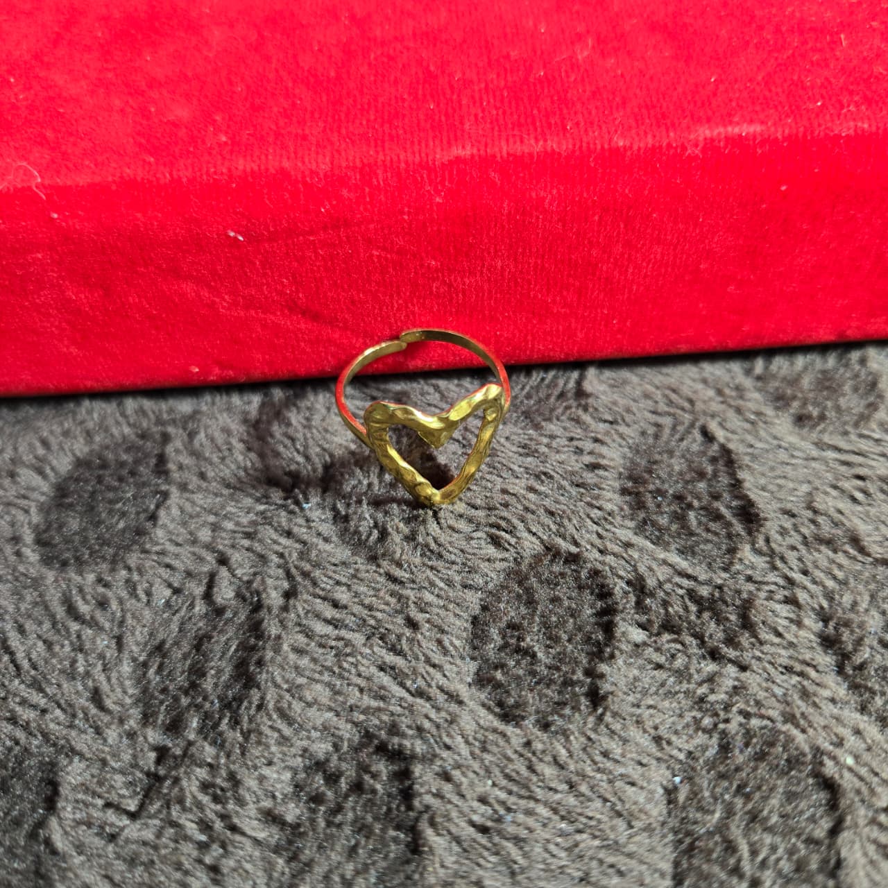 Gold heart-shaped ring on a textured gray surface with a red box in the background