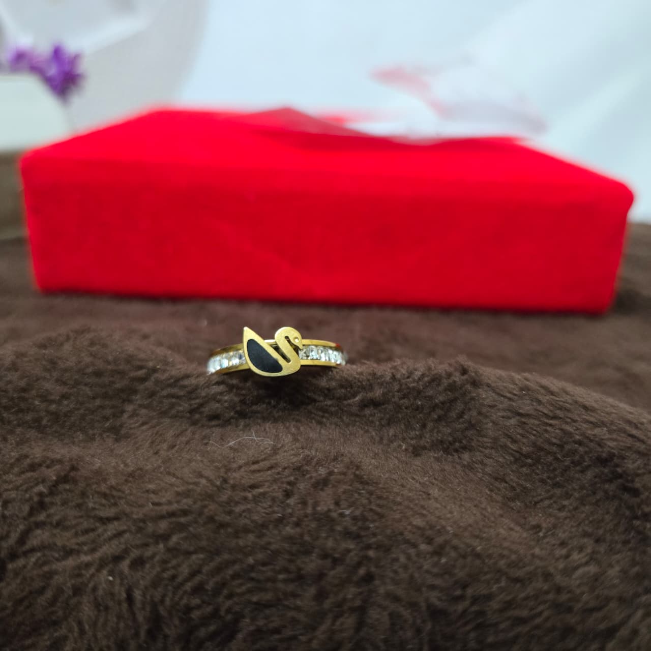 Gold ring with black stone on a brown surface with a red box in the background