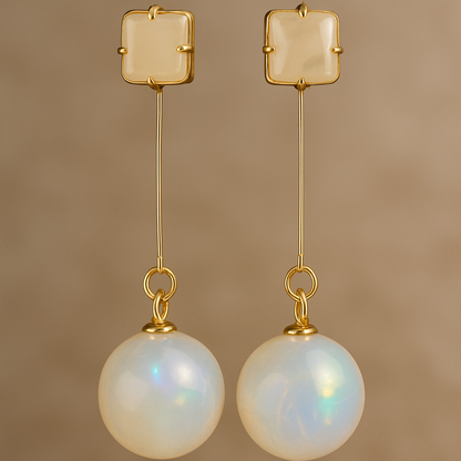 Pair of gold earrings with round pearl-like beads on a beige background