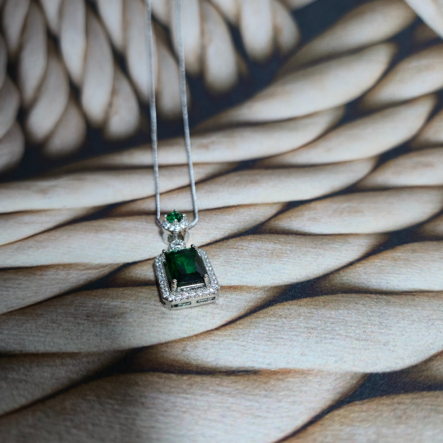 Green gemstone pendant on a silver chain against a woven background