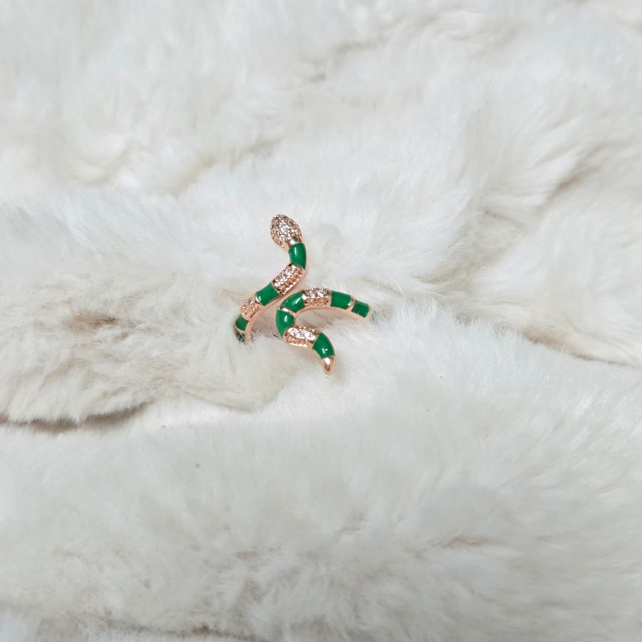 Rose gold and green snake-shaped brooch on a white fur background