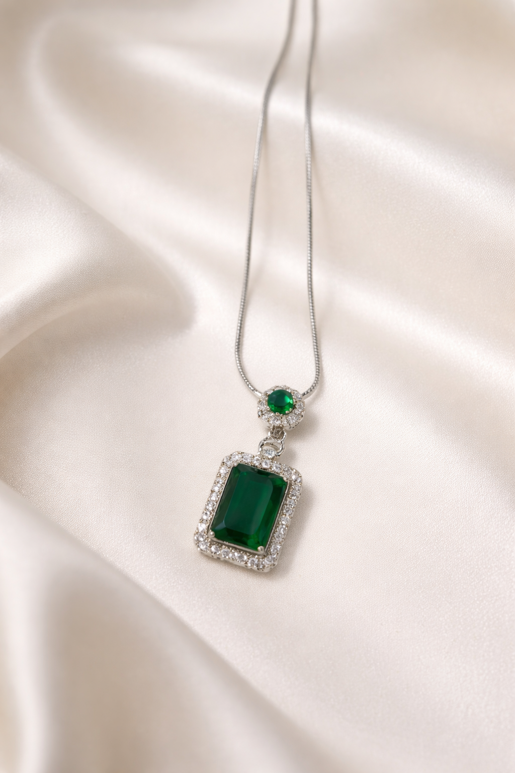 Green gemstone pendant on a silver chain against a cloth background