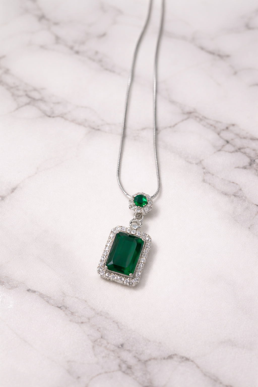 Green gemstone pendant on a silver chain against a white background