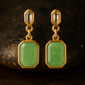 Gold earrings with green gemstones on a dark background