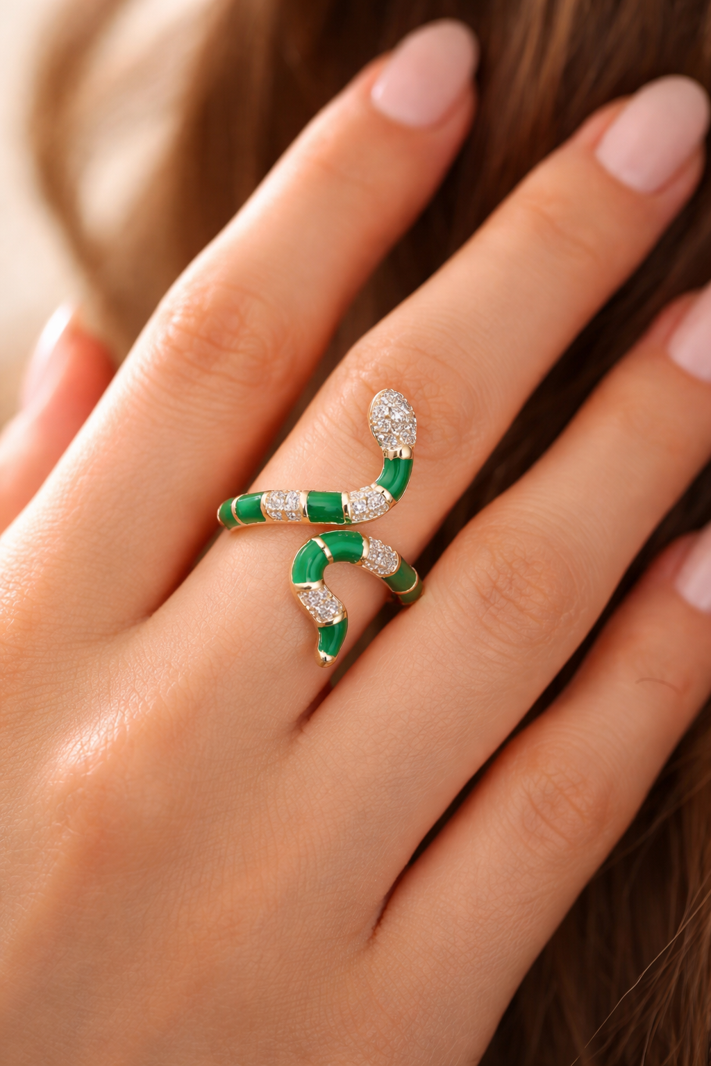 Rose gold and green snake-shaped brooch on a woman's finger.