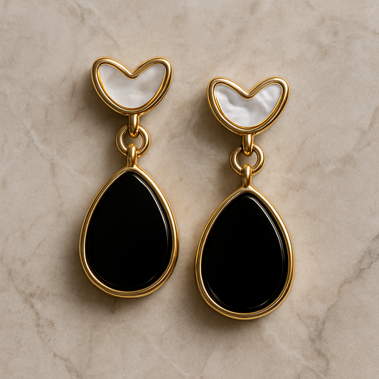 Gold earrings with black teardrop stones and white heart-shaped tops on a beige marble background