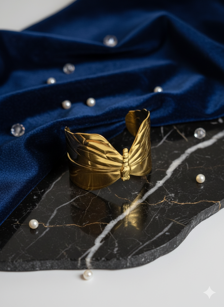 Gold butterfly-shaped earring on a black marble surface with blue fabric and pearls in the background