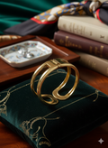 Gold ring on a green cushion with books and decorative items in the background