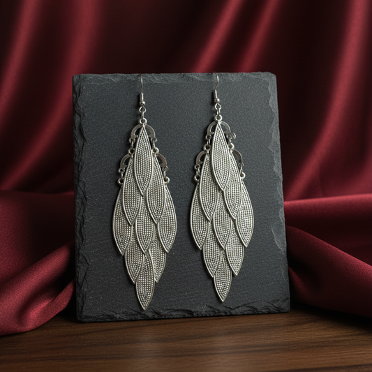 Silver leaf-shaped earrings on a dark slate against a red satin background