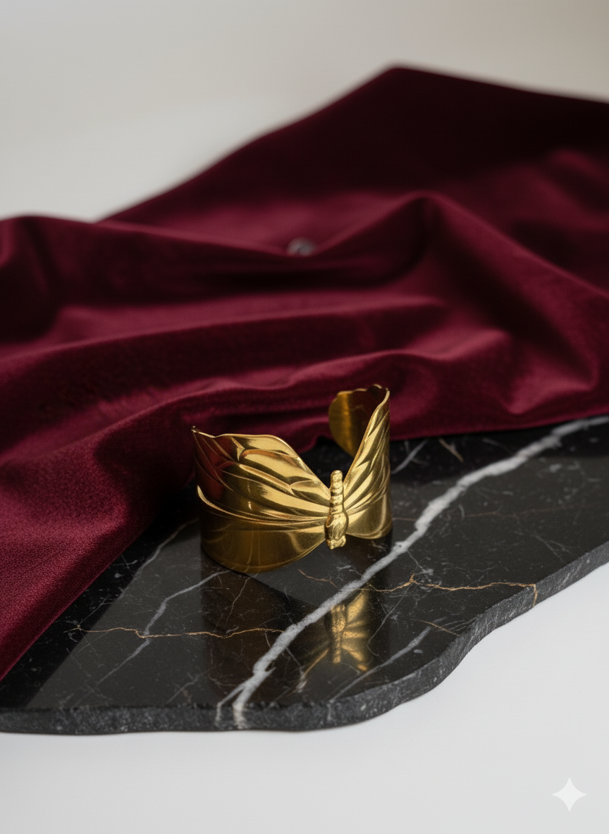 Gold butterfly-shaped object on a black marble surface with red fabric in the background