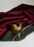 Gold butterfly-shaped object on a black marble surface with red fabric in the background