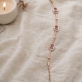a bracelet with rose-gold toned bracelet featuring elegant crystal-studded emblem charms on a white cloth. 