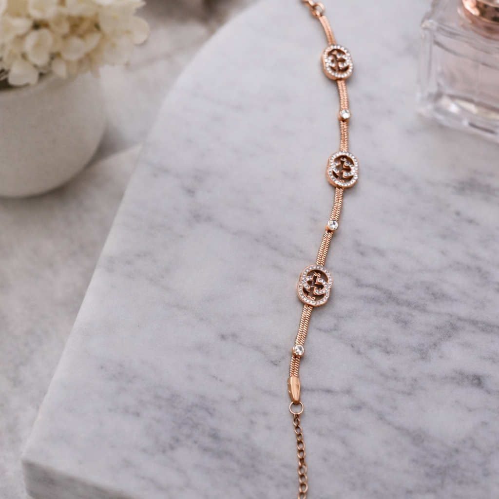 a bracelet with rose-gold toned bracelet featuring elegant crystal-studded emblem charms on a white cloth. 