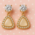 Gold earrings with beige stones and clear gemstones on a pink polka dot background
