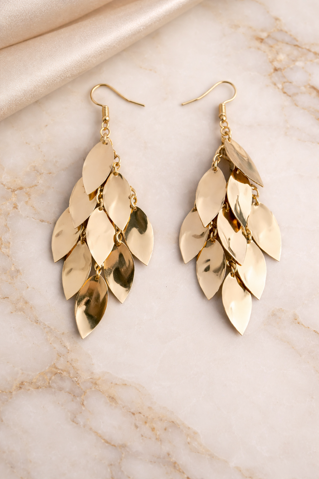 Gold leaf-shaped earrings on a marble background