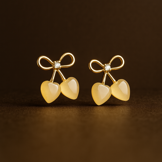 Gold-tone stud earrings featuring a bow design with a central crystal and two heart-shaped stone drops, resembling cherries.