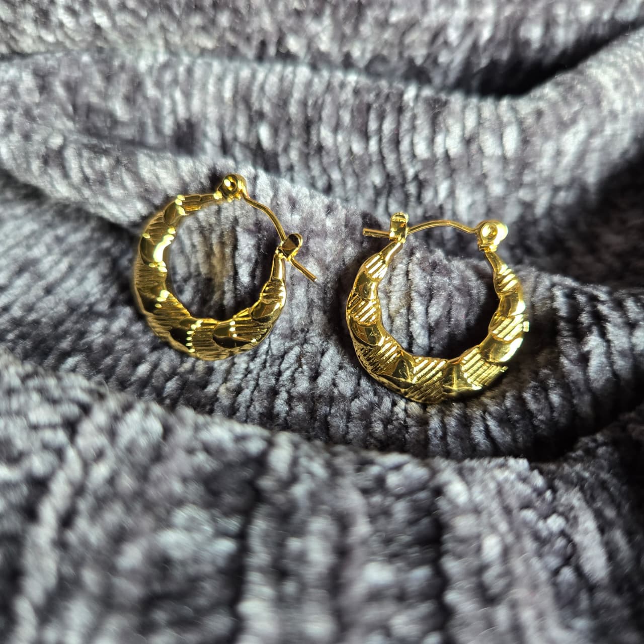 Gold hoop earrings on a textured gray fabric background