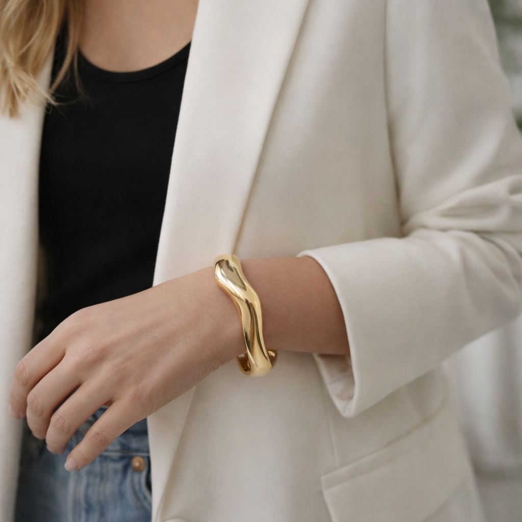 a sleek gold bangle designed with smooth flowing curves on a woman's arm.